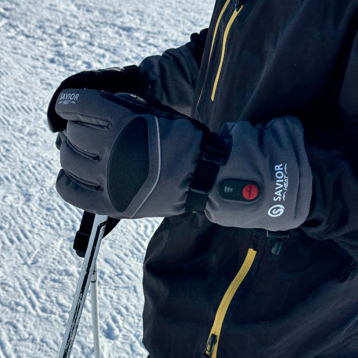 Skier holding poles on snowy terrain wearing gray waterproof heated gloves with temperature control, showing winter outdoor performance.