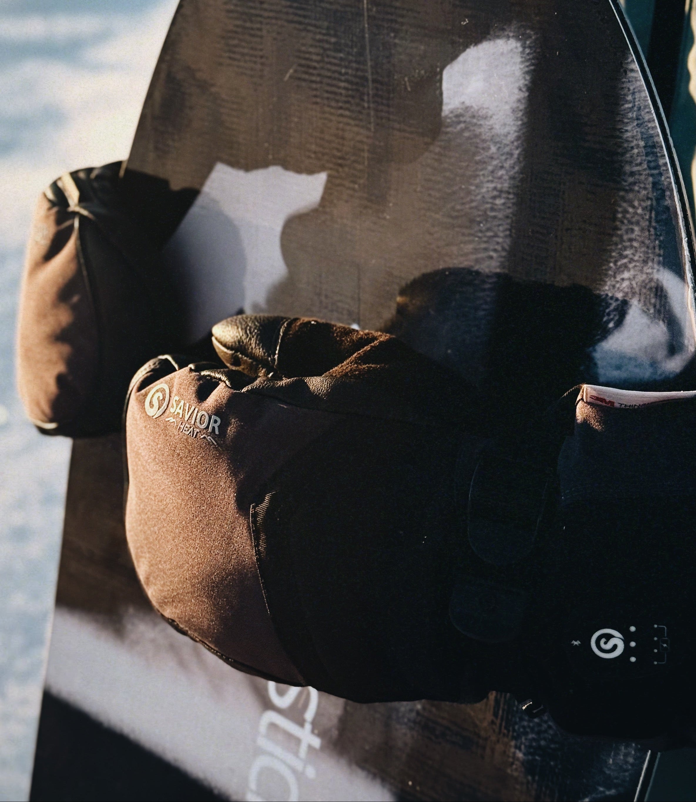 Close-up of battery heated gloves gripping a snowboard at sunrise, highlighting winter warmth, insulation, and outdoor performance.