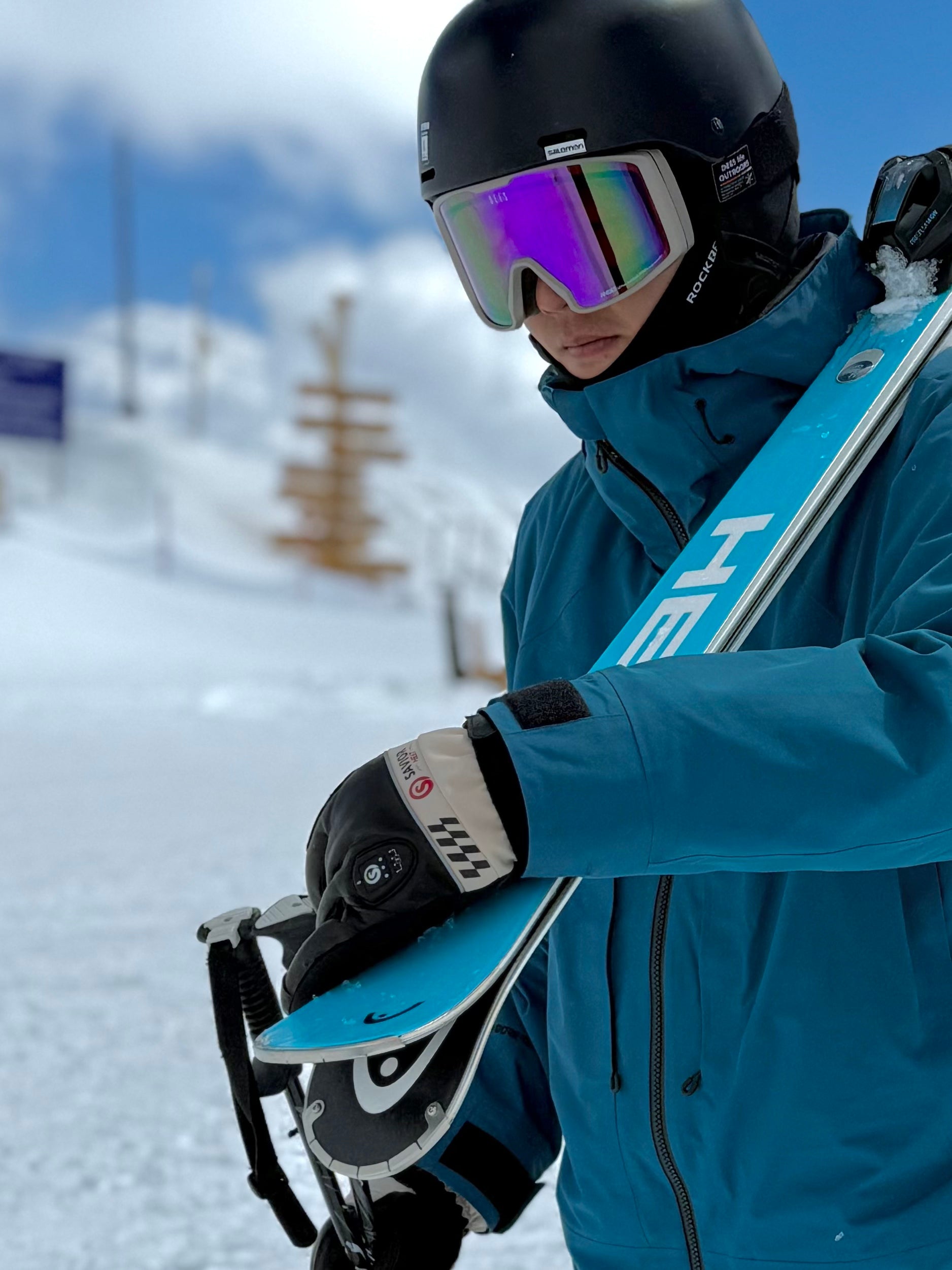 Skier adjusting skis in cold weather while wearing battery heated gloves, showing reliable warmth and performance during winter mountain activity.