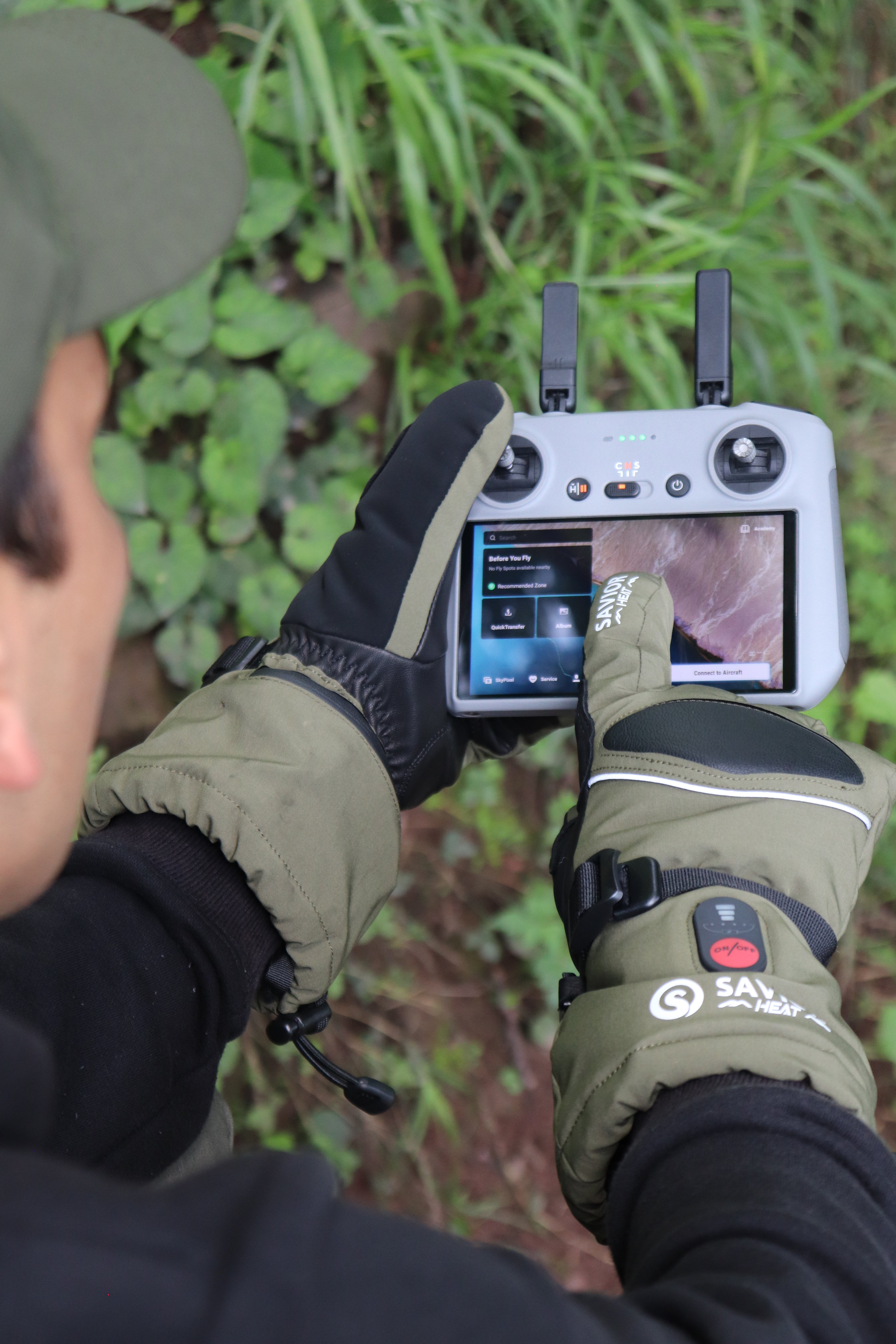 Person using a drone controller while wearing touchscreen heated gloves outdoors.
