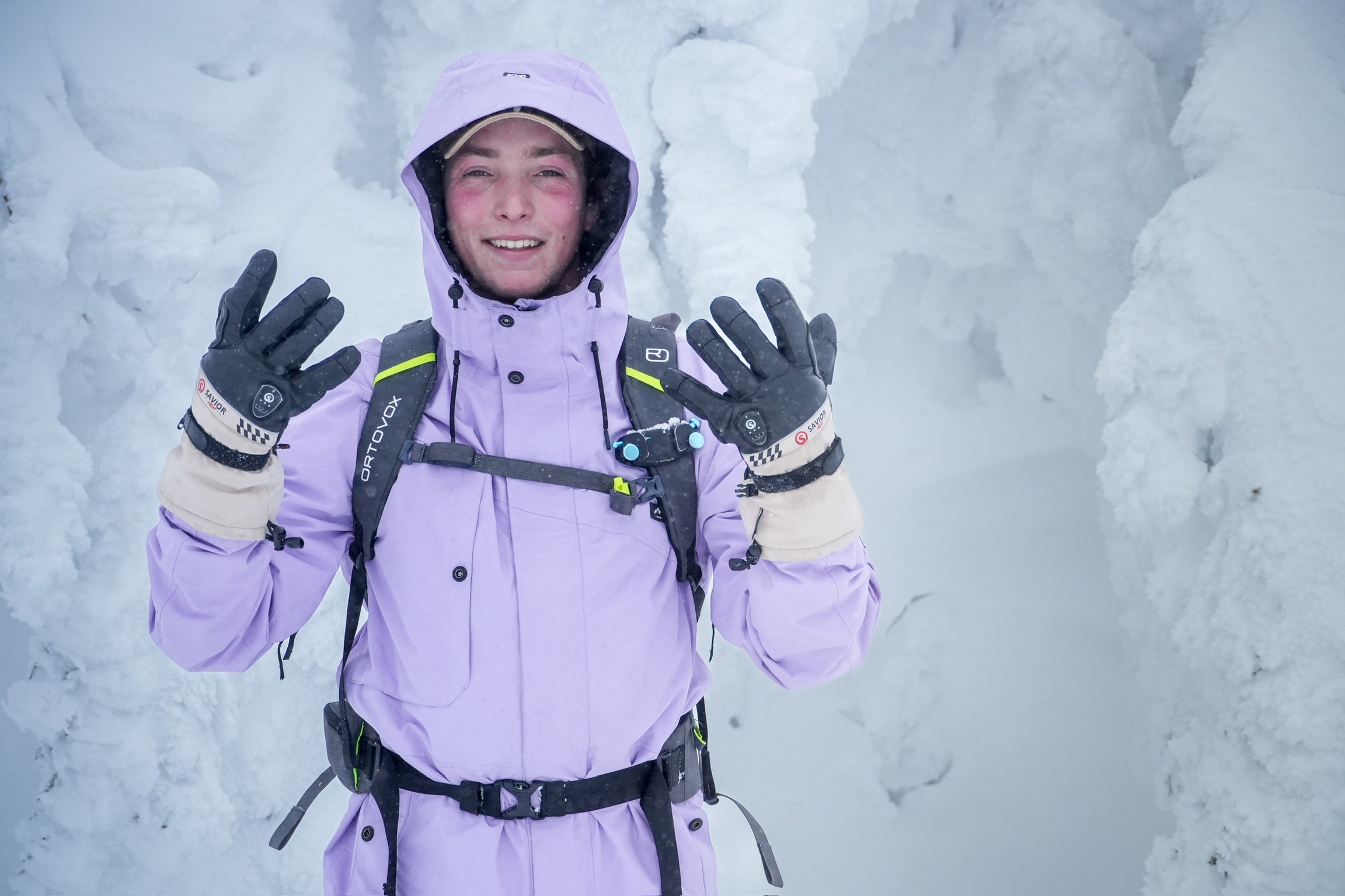 Smiling skier in snowy terrain wearing insulated winter gloves, lifting hands to show warmth and protection in extreme cold conditions.