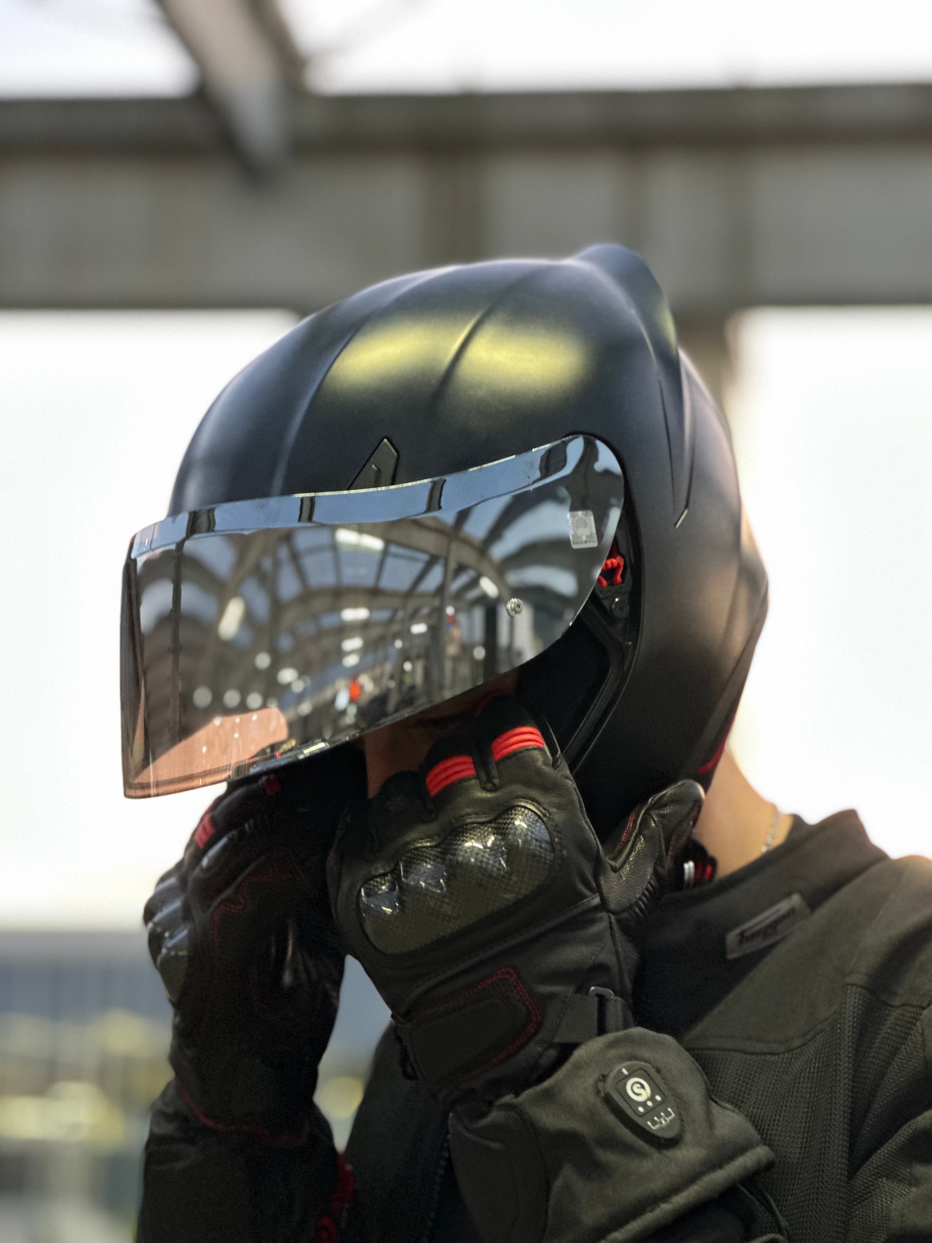 Rider adjusting a reflective motorcycle helmet while wearing heated protective motorcycle gloves.