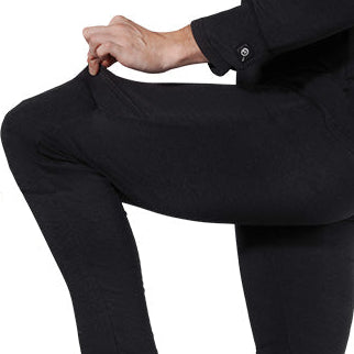 Person wearing black heated thermal pants, stretching the fabric at the knee with a visible power button on the cuff.