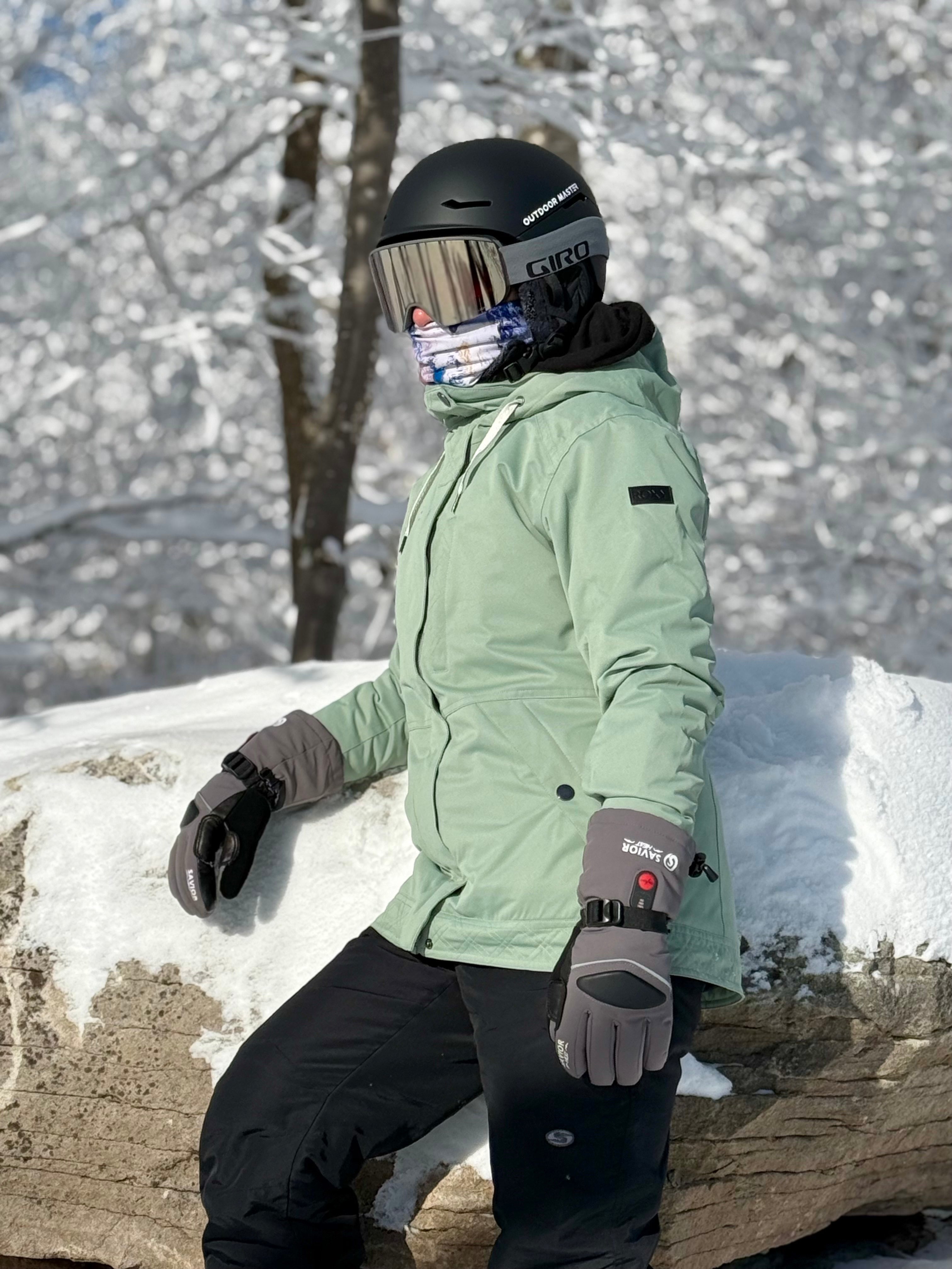 Skier wearing windproof heated gloves while resting in snowy terrain, showing durable winter protection for cold-weather skiing and outdoor activities.