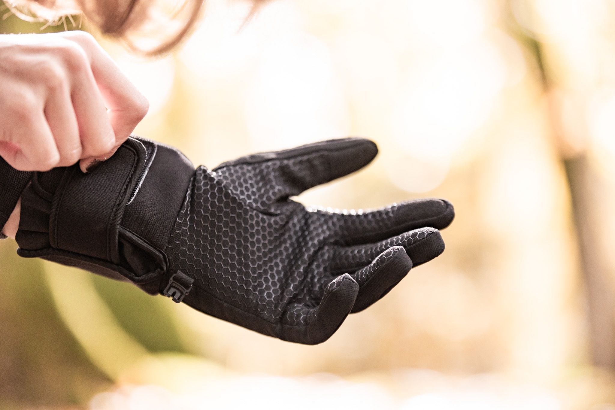 Close-up of heated gloves with anti-slip palm texture being adjusted for outdoor use.