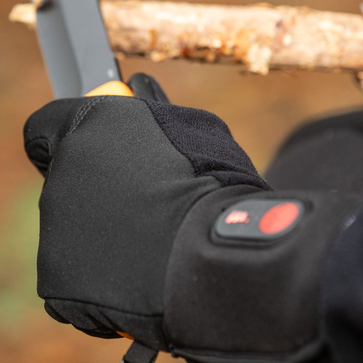 Gloved hand using a knife to trim a wooden branch during an outdoor task in the forest.