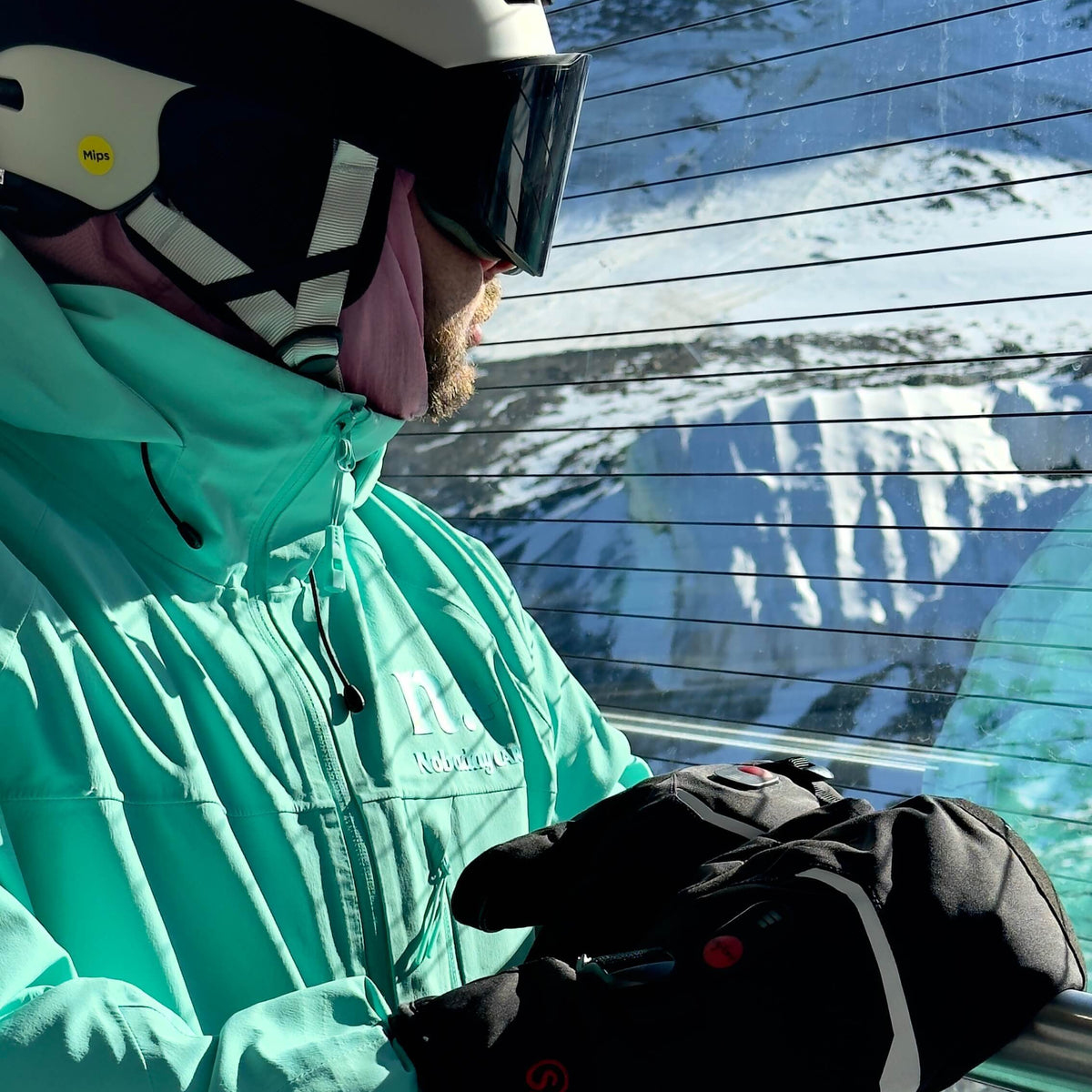 Skier wearing best heated ski gloves on chairlift in mint green jacket and white helmet