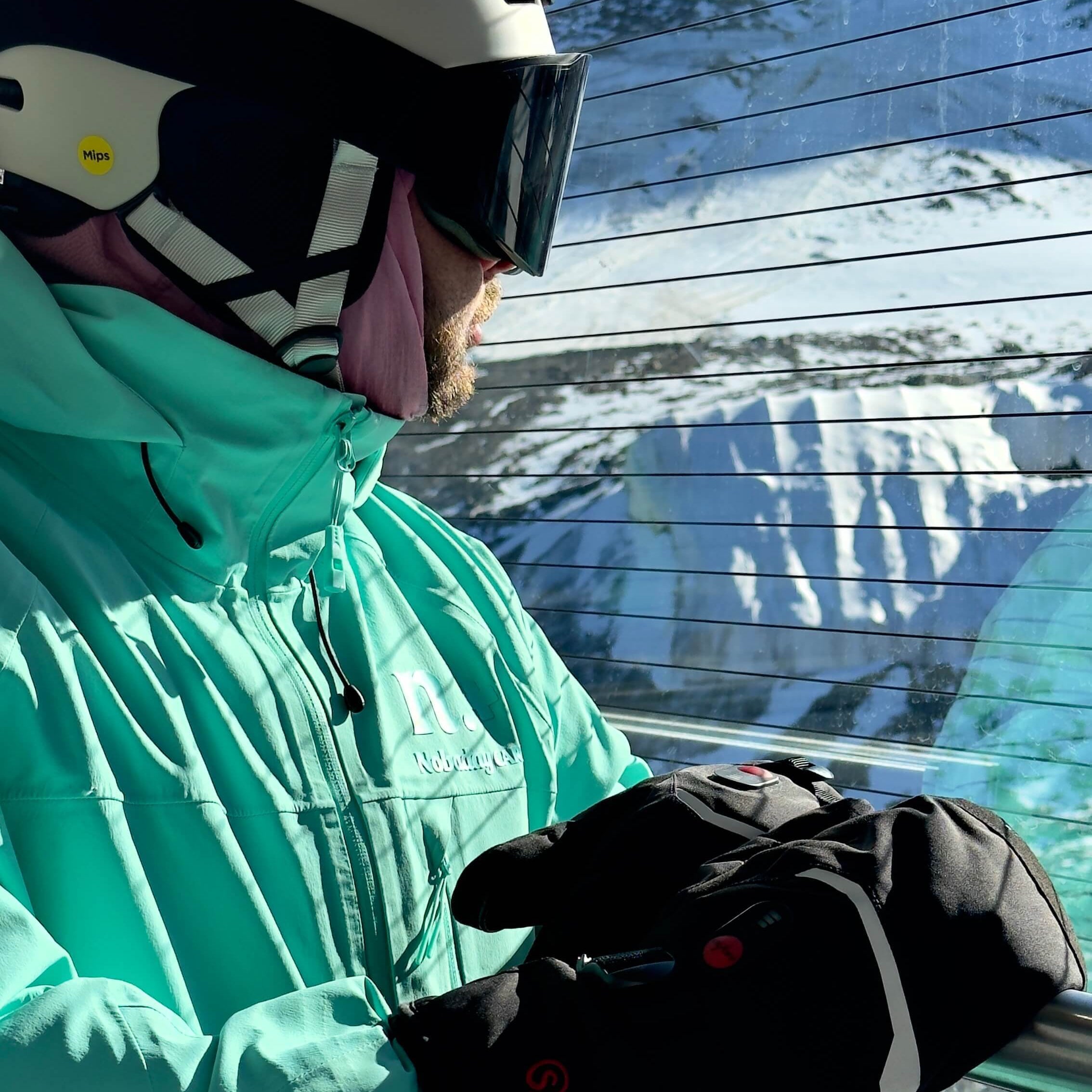 Skier wearing best heated ski gloves on chairlift in mint green jacket and white helmet